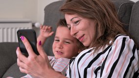 Mother and son using mobile phone on sofa at home. High quality 4k footage