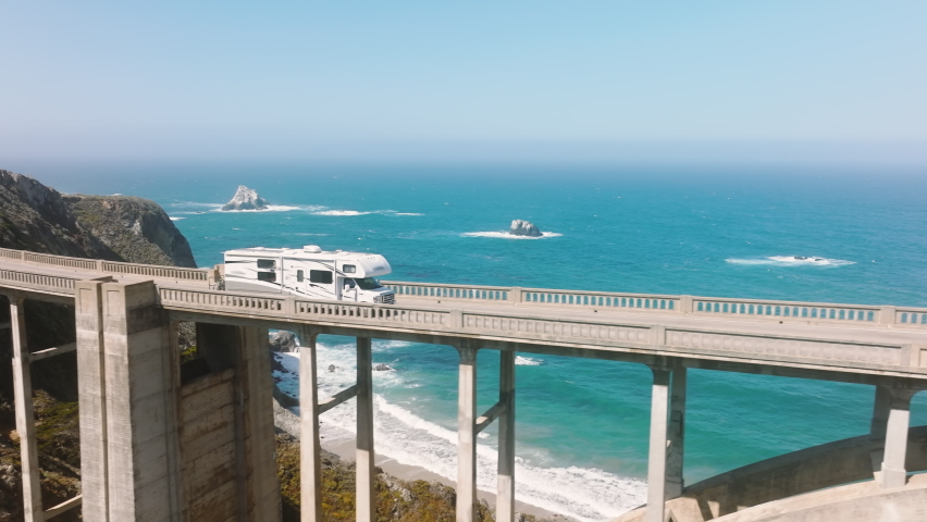 Aerial RV driving by road on American road trip with cinematic ocean background. Scenic beautiful drone footage of famous Bixby bridge. Tourist exploring nature. Family vacation travel RV holiday trip Royalty-Free Stock Footage #1093913431