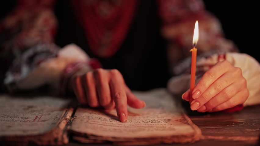 Ukrainian woman reading ancient book - Bible. Concentrated attentively follows finger on paper page under candle light. History of Kyiv Rus. Psalter, 19th century, prayers and psalms