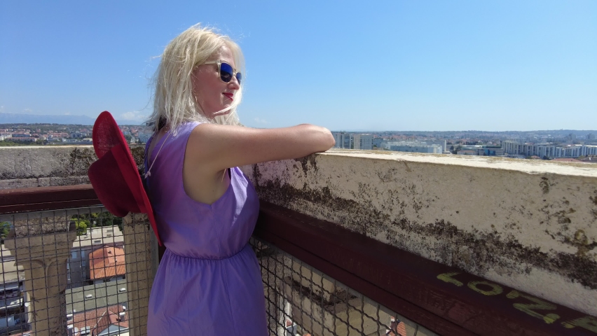 elegant girl with red hat on top of Zadar bell tower of cathedral sv. Stosije. Panoramic terrace view on Zadar city skyline in summer. Croatian city on Adriatic Sea and Zadar capital of Dalmatia.