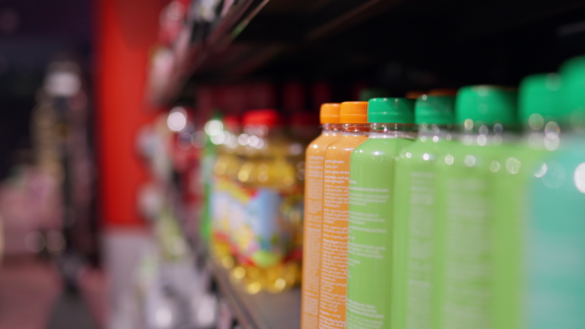 The hand of a young caucasian woman takes a bottle of a drink from a supermarket shelf, Buying store products, shopping, spending money, Drink in a bright plastic bottle on a shelf in a supermarket
 Royalty-Free Stock Footage #1093915799