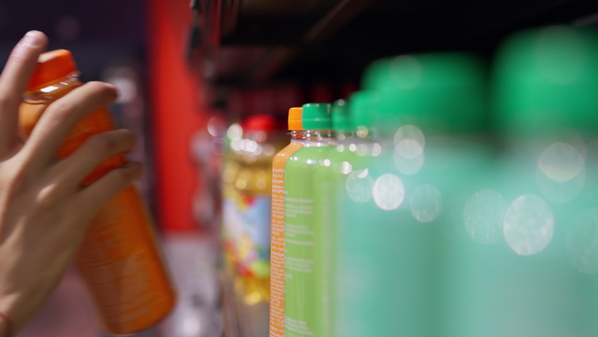 The hand of a young caucasian woman takes a bottle of a drink from a supermarket shelf, Buying store products, shopping, spending money, Drink in a bright plastic bottle on a shelf in a supermarket
 | Shutterstock HD Video #1093915799