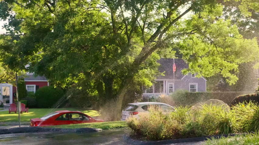 Rotating Sprinkler Watering a Fenced in Yard Passing Through the Sun Near Sunset and american flag in the suburbs. Wide view