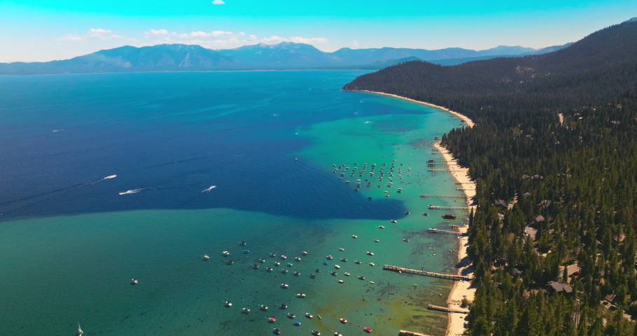 Stunning turquoise scenery of Lake Tahoe with boats sailing on. Huge forest of pine trees covering the land. Top view.