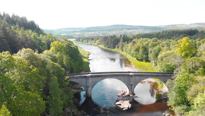 Stone bridge across river in highland nature of Scotland, sunny, drone.