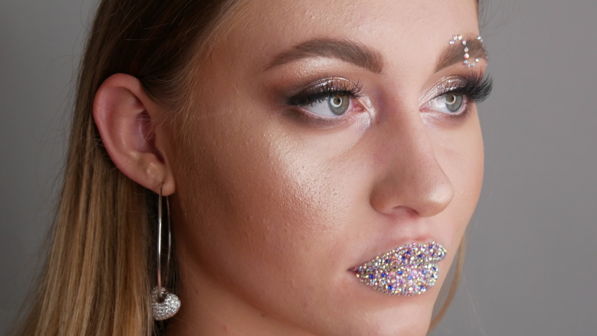 Portrait of a beautiful young girl model in stylish evening make up smoky eyes posing. Fashion style in makeup, a girl with lips on which various rhinestones