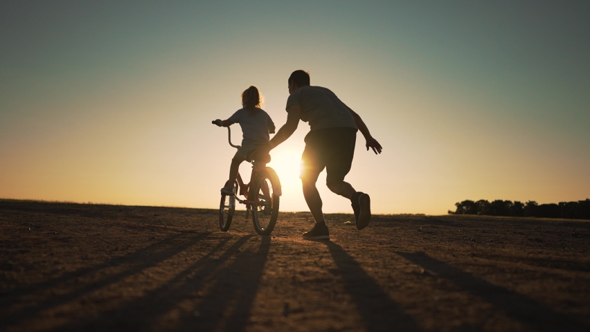 Happy family. Father teaches daughter to ride bike in park. Daughter riding bike for first time. Kid dream of traveling by bike. Girl is learning to ride a bike. Father helping hand to daughter. | Shutterstock HD Video #1093929207