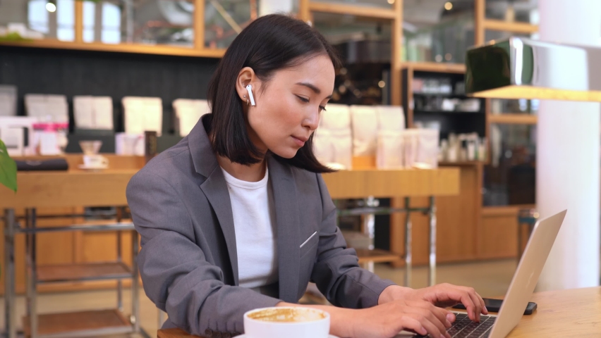 Busy smart young Asian professional business woman using laptop computer drinking coffee during lunch in cafe. Korean lady entrepreneur or manager remote distance working online watching webinars. Royalty-Free Stock Footage #1093931909