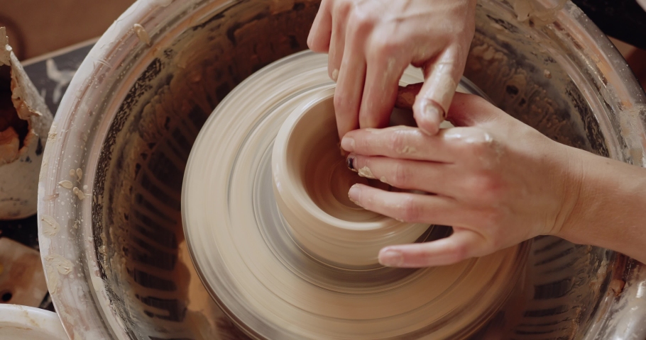 Cropped view of the female making clay pot on the ceramic wheel. Pottery girl is engaged in sculpting. Handicraft production, clay work concept 