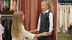 Mother and daughter are standing in the store opposite the fitting room. Girl trying on a school dress. Slow motion video