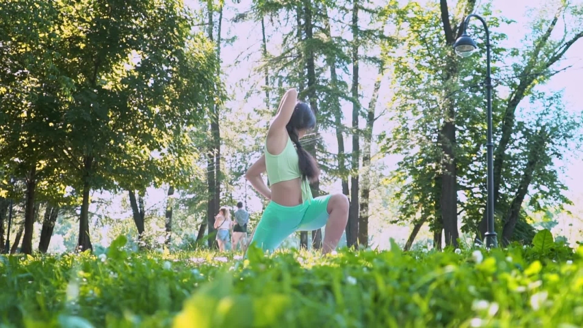 Meditating outdoors beautiful young yogi woman enjoying relaxing on a green meadow in sunny weather. The concept of a healthy lifestyle, slow motion, doing sports in an urban environment