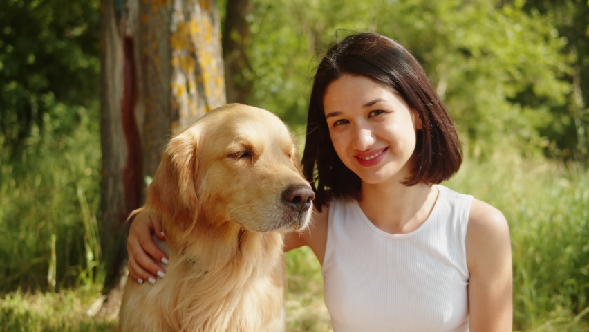 Woman petting golden retriever, young pet owner portrait. Female handler stroking labrador close-up, walking together in forest. Happy dog puppy.  Royalty-Free Stock Footage #1093942515