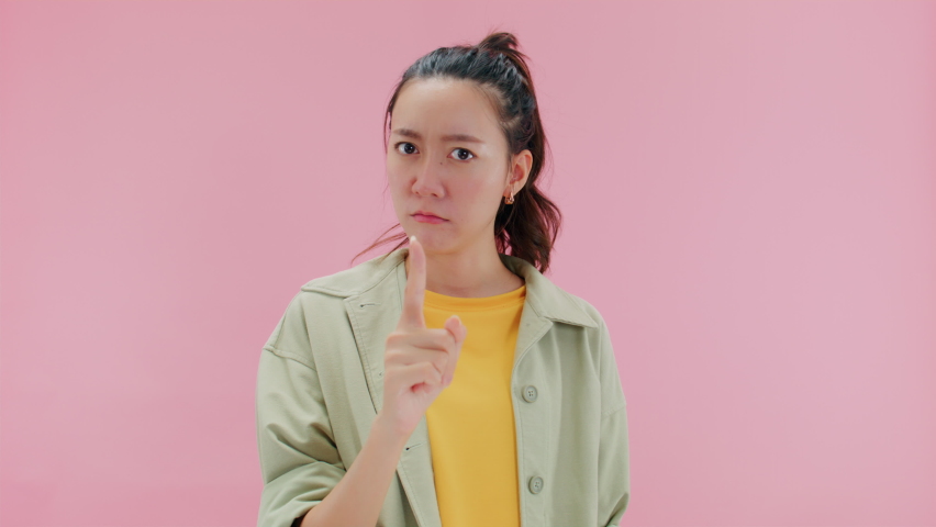 SAY NO, Serious young asian woman doing warning or disapproving sign, don't do it, I don't need it or not allowed with finger shaking admonishing gesture looking at camera.Isolated on Pink Background