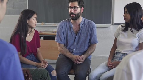 Confident young male mentor teacher talking to multiracial students - Teenagers sitting in a circle having a group discussion in High School classroom – Video có sẵn