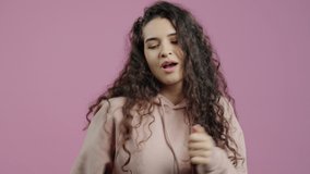 Slow motion portrait of happy girl dancing and smiling enjoying music on pink background. Carefree youth and entertainment concept.