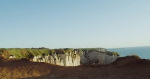 A young woman walks between a green meadow on top of a sheer cliff, admiring the opening view of the English Channel and the chalk cliffs. Etretat, France. 4k video, red komodo
