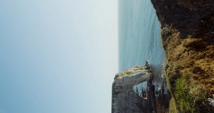 A young woman walks on a hilltop with a beautiful view of sheer cliffs with a picturesque natural arch, washed by the waters of the English Channel. Etretat, France. 4k vertical video. 3D Illustration