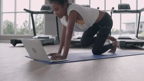 Fitness young black woman doing exercise yoga in gym. African american female loook at laptop computer lesson practicing Yaga plank pose on social online internet class. Healthy lifestyle concept.