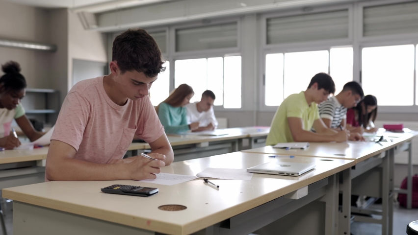 Group of college students doing an exam sitting in a row in class. Teenage guys and girls studying at high school. Education and final test concept. High quality 4k footage Royalty-Free Stock Footage #1093951907
