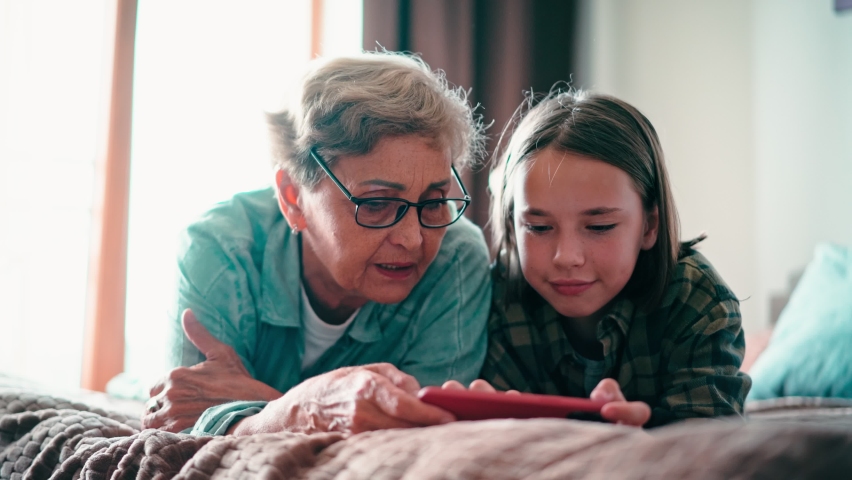 Happy grandmother and her granddaughter using a cellphone together, playing a game. A senior woman and a child girl are having fun. Royalty-Free Stock Footage #1093952805