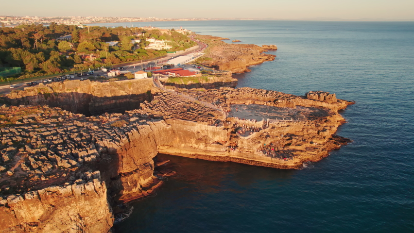 Aerial drone footage of the rocky coast by the sea in Cascais town at sunset, Lisbon, Portugal. Natural landmark Boca do Inferno or Hell's mouth in Cascais city. Orbit shot Royalty-Free Stock Footage #1093961587