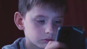 portrait of a caucasian boy 7-8 years old attentively looking at the screen of a smartphone that he holds in his hands. the child reads the news, uses social networks and surfs online using the phone