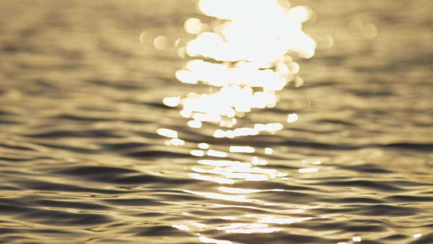 Slow motion shot of sea water surface at sunset. Reflection of golden sunlight over the sea or ocean