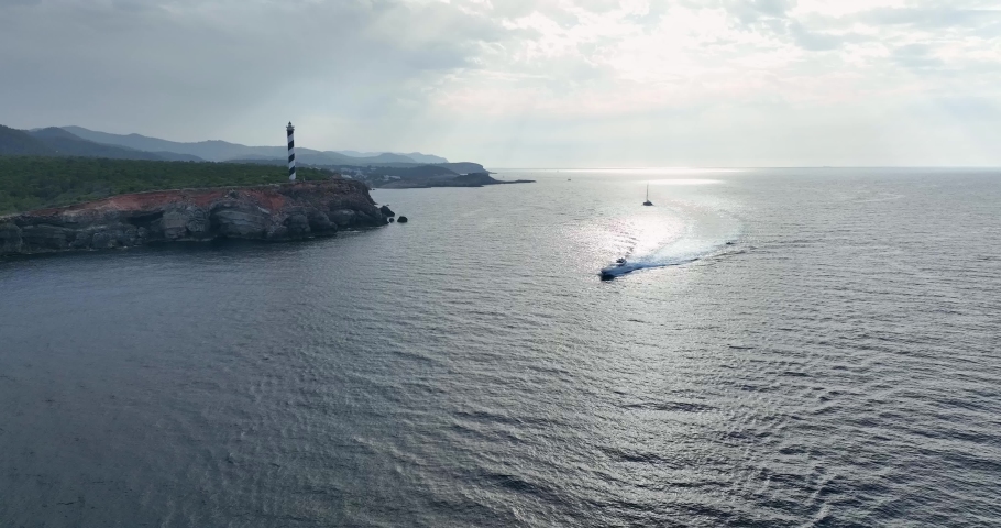 Lighthouse on top of a cliff facing the sea, surrounded by a large forest on a day about to rain.