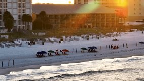 Aerial video of Destin Beach. Emerald coast green waters. Tide coming in with rainbow sun glare. Setting up beach chairs and umbrellas.