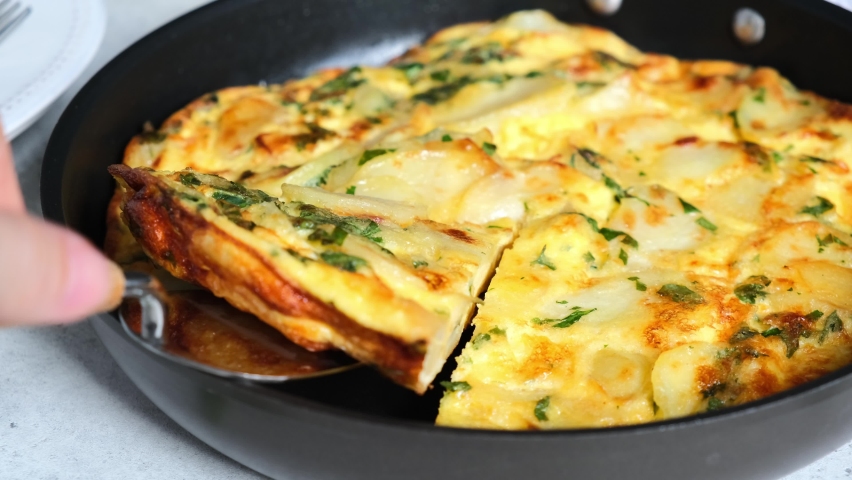 Traditional Spanish potato tortilla or omelette in black pan.