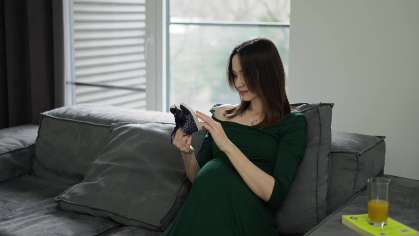 Happy woman walking baby shoes on her pregnant belly at home on sofa | Shutterstock HD Video #1093989183