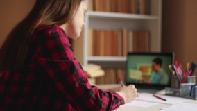 distance learning online education. girl student studying at home on a laptop watching an online seminar near a bookcase desk. distance online education concept. teen girl on an school online exam