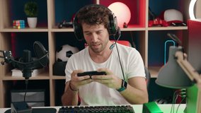 Young hispanic man streamer playing video game using smartphone at music studio