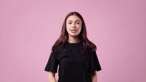 4k video of positive woman in a balck T-shirt with raised arms and a smile on pink background.