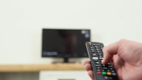 Man's hand selects internet tv channels with remote control, close-up. Person controls TV using a modern remote control. A man watches smart TV and uses black remote control