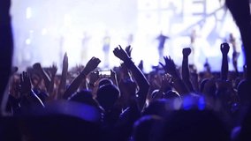 People silhouettes jump waving hands, taking photos or recording videos of live music concert with smartphones at open air festival. Bright colorful stage lighting. Fans at favourite band performance.