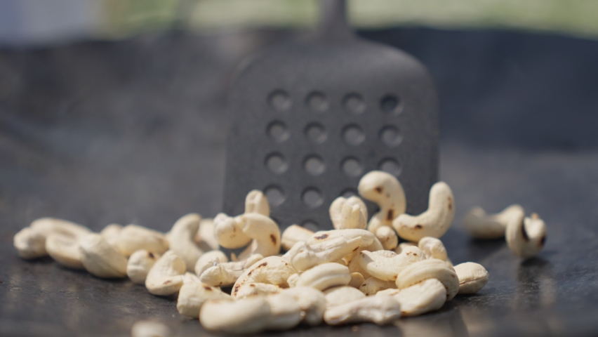 Cashew nuts roasting on cast iron pan of rustic stove. Nuts on fire, roast and mix the Indian nuts.