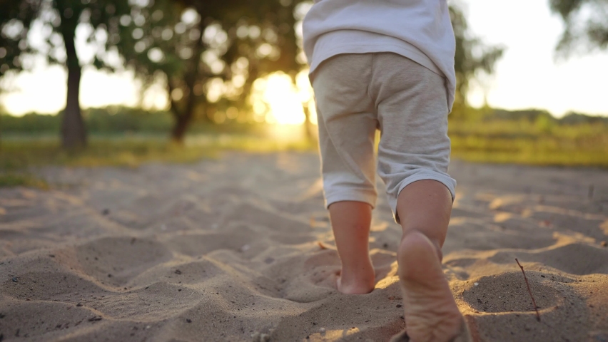 baby run in the park on the sand. bare feet child son run on the sand in the park near the water. happy family kid dream concept. childhood joy baby kid run in the park fun