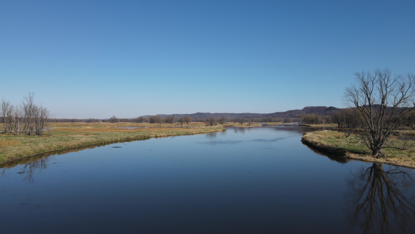 Wide landscape view of waterways in Wisconsin in autumn. Calm glistening water. Reflections from the sun on the water. Bare trees dotting the island. Patches of green grass