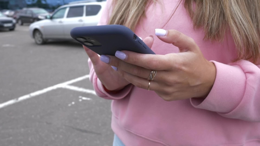 The girl communicates on her smartphone by tapping on the screen while standing in the parking lot at the shopping center. People and technology. | Shutterstock HD Video #1094004965