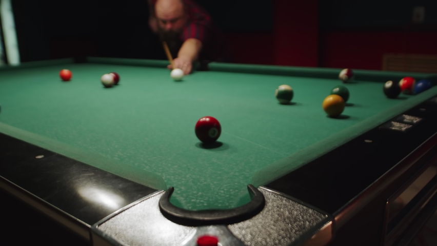 Overweight caucasian pool player enjoying sports game of billiard. Sinking red ball number seven into a pocket. Pool balls scattered on a green table. | Shutterstock HD Video #1094007497