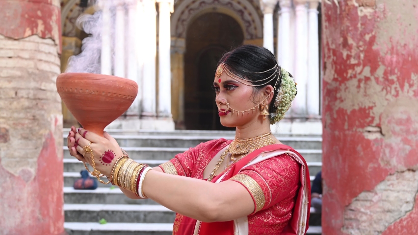 Shot of a Bengali woman wearing red and white sari dancing with holding Dhunachi emitting incense during Durga puja festival in Kolkata, West Bengal. Royalty-Free Stock Footage #1094008571