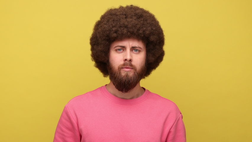 Bearded hipster man with Afro hairstyle looking at camera and nodding yes, showing approving gesture, body language concept, wearing pink sweatshirt. Indoor studio shot isolated on yellow background. | Shutterstock HD Video #1094009197