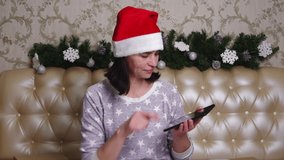 A woman in a Santa hat is looking for gifts for Christmas and New Year in an application on a smartphone. Shopaholic woman searches for goods on the Internet. Christmas online shopping concept