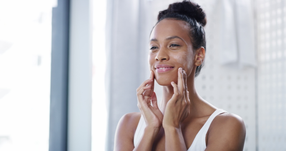Skincare, face and cosmetic cream of a black woman using facial beauty products for morning self care. Skin care of African female with a smile happy skin health and wellness in a home bathroom