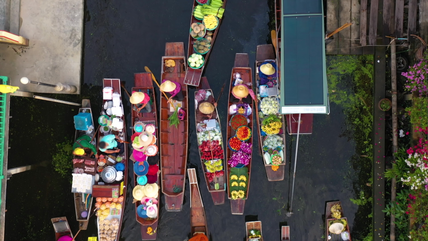 Top view from drone of famous and exotic floating market at Damnoen Saduak canal. Plenty of fresh fruits, vegetables, flowers and street food available to buy in rural village. traditional of folks.  | Shutterstock HD Video #1094021137