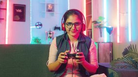 Excited woman celebrating for win while playig video game on sofa using game pad by looking camera at home - concept of leisure activities, entertainment and happiness.