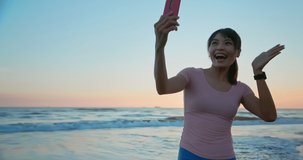 asian woman has video chatting with friends or family through mobile phone on beach in dusk