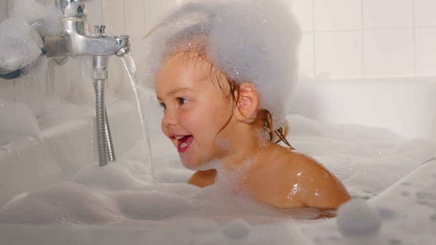 A little cheerful girl washes and plays in the bath with foam. Daily hygiene and skin care of children. Playing with water. Baby shampoo soap Royalty-Free Stock Footage #1094027865