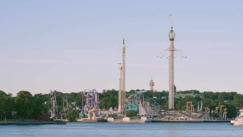 Amusement park Gröna Lund in Stockholm Sweden with tourists boats passing by in city center. Attraction such as roller coaster rides, giant wave swinger, freefall giant high drop tower. 